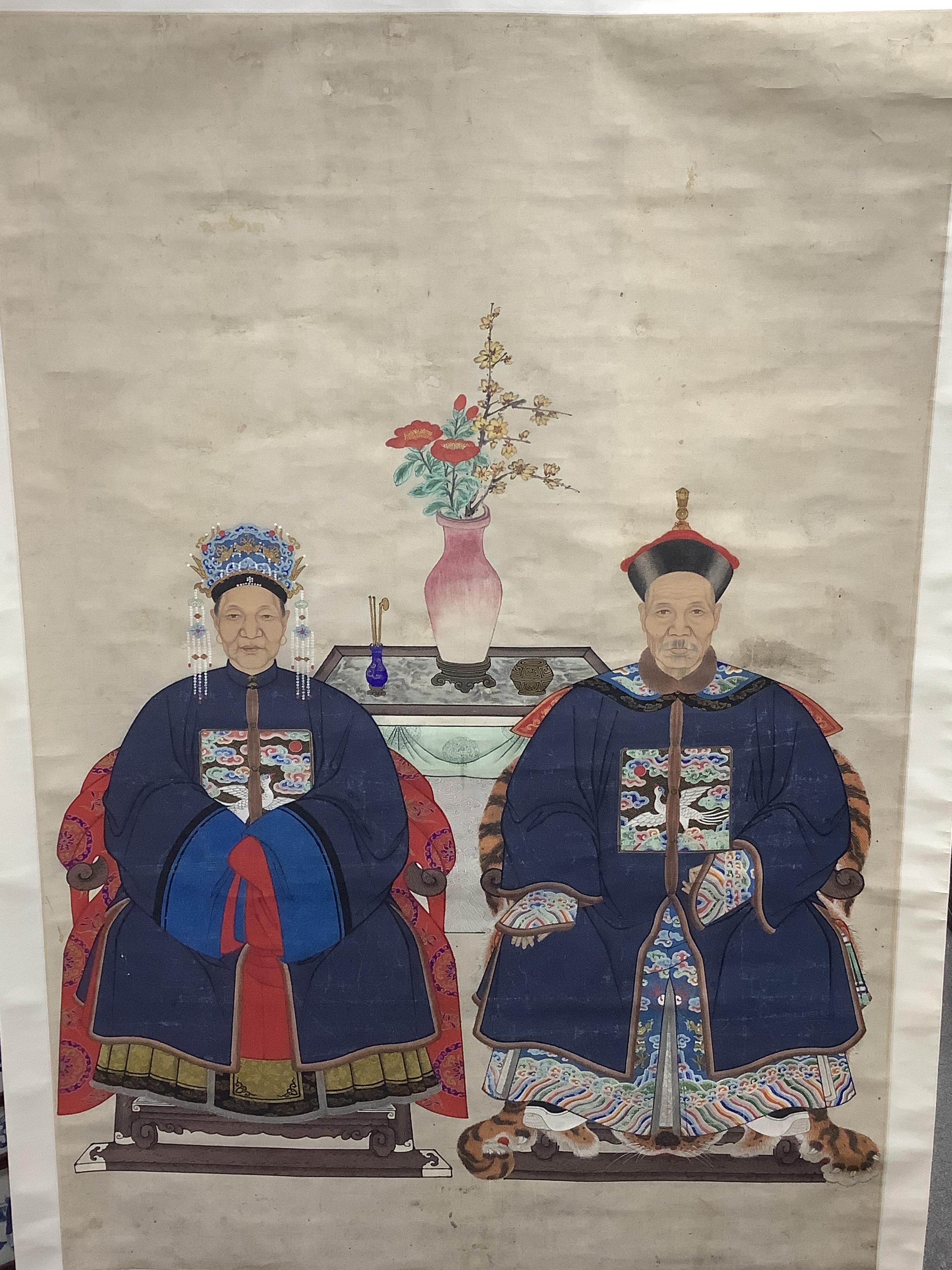 A Chinese ancestor scroll painting on paper, late Qing dynasty, depicting a husband and wife, wearing formal robes, seated on thrones, with a table and scholarly objects behind them, image 132cm x 91cm, later mounted